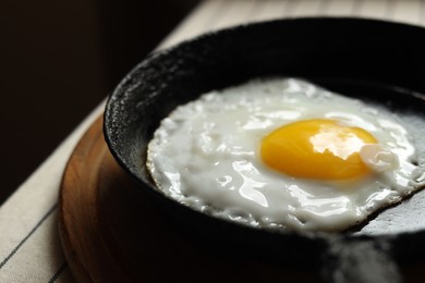 Frying pan with tasty cooked egg on wooden board, closeup