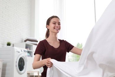 Young woman with clean bedsheet indoors. Laundry day
