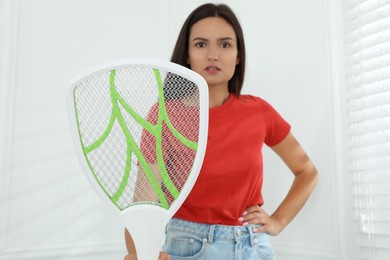 Photo of Young woman with electric fly swatter indoors, focus on device. Insect killer