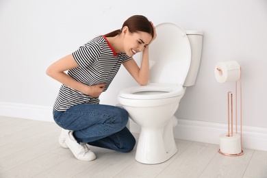 Young woman suffering from nausea over toilet bowl indoors