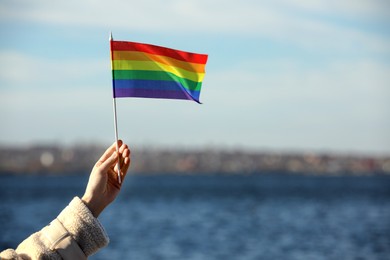 Woman holding bright LGBT flag near river, closeup. Space for text