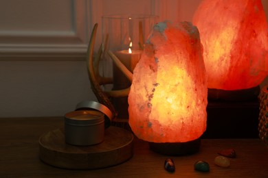 Himalayan salt lamps, candle and gemstones on wooden table near white wall indoors