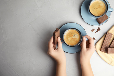 Woman having breakfast with cup of delicious coffee and wafer at grey table, top view