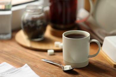 Cup of freshly brewed tea and spoon with sugar on wooden table, space for text