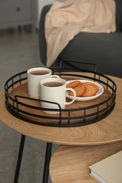 Photo of Tray with cups of hot tea and cookies on wooden table in living room. Interior design