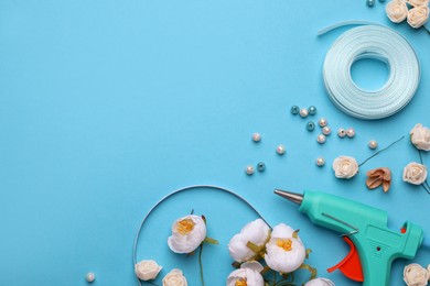 Hot glue gun, plastic headband and handicraft materials on light blue background, flat lay. Space for text