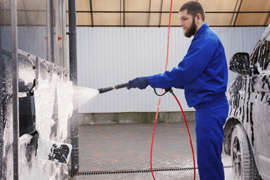 Worker cleaning automobile floor mats with high pressure water jet at car wash