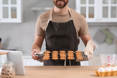 Man holding grid with freshly baked cookies in kitchen, closeup. Online cooking course