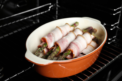 Uncooked bacon wrapped asparagus in baking dish on oven rack, closeup