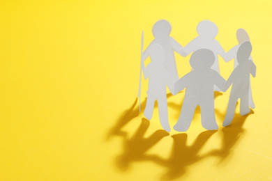 Paper people chain making circle on yellow background, space for text. Unity concept
