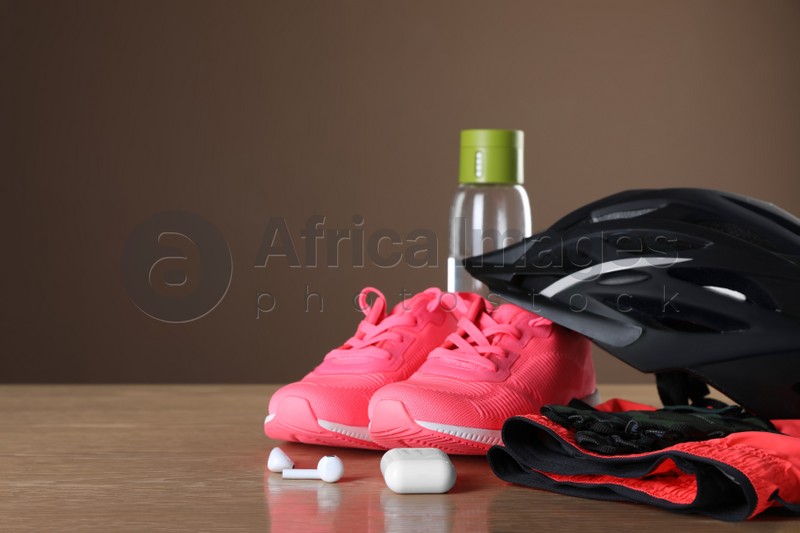 Different cycling accessories on wooden table against brown background, space for text