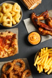 Photo of French fries, onion rings and other fast food on black table, flat lay