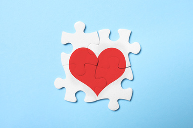 Concept of love. White puzzle pieces with illustration of heart on light blue background, top view