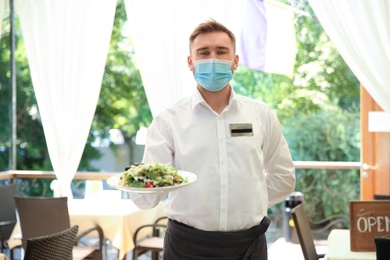 Waiter with plate of salad in restaurant. Catering during coronavirus quarantine