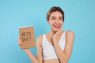 Woman holding notebook with phrase Keto Diet on light blue background