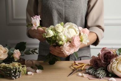 Florist creating beautiful bouquet at wooden table indoors, closeup