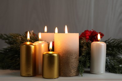 Different burning candles and Christmas decor on white wooden table