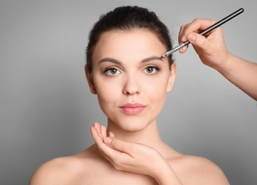 Visage artist applying makeup on woman's face against grey background. Professional cosmetic products
