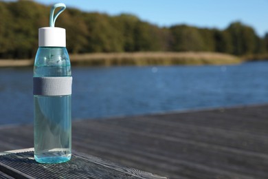 Glass bottle with water on wooden pier near river outdoors. Space for text