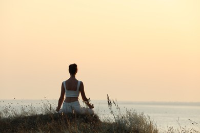 Photo of Woman meditating on hill near sea, back view. Space for text