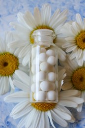 Bottle of homeopathic remedy and beautiful chamomiles on color background, closeup. Top view