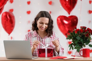 Photo of Valentine's day celebration in long distance relationship. Woman opening gift from her boyfriend indoors