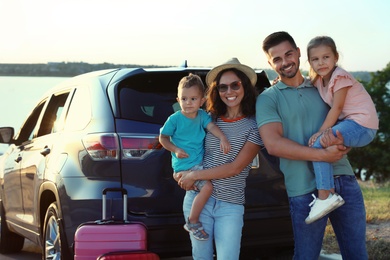 Happy family with suitcases near car on riverside