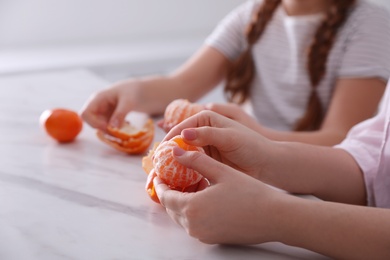 Girls peeling fresh tangerines at table in kitchen, closeup