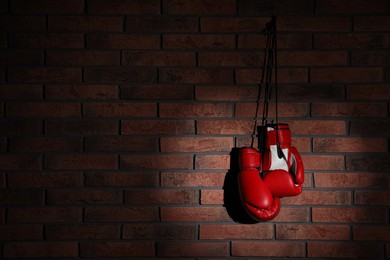 Pair of red boxing gloves hanging in spotlight on brick wall, space for text