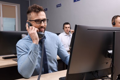 Handsome call center operator talking on phone and his colleagues working in modern office