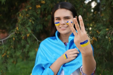 Photo of Young woman showing Ukrainian trident gesture outdoors, focus on hand. Space for text