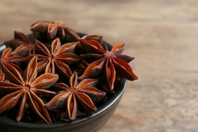Bowl of aromatic anise stars on wooden table, closeup. Space for text
