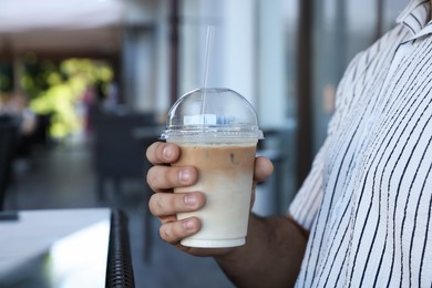 Photo of Man with plastic takeaway cup of delicious iced coffee in outdoor cafe, closeup