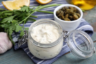 Photo of Tasty tartar sauce in glass jar and ingredients on light blue wooden table