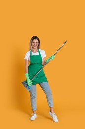 Young woman with broom on orange background
