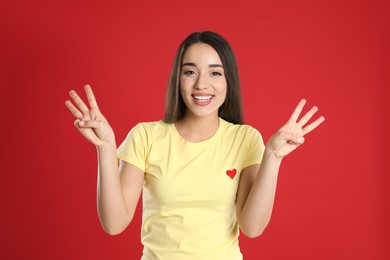 Woman in yellow t-shirt showing number six with her hands on red background