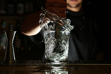 Bartender preparing fresh alcoholic cocktail at bar counter, focus on glass