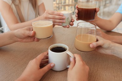 Photo of Friends drinking coffee at wooden table in cafe, closeup
