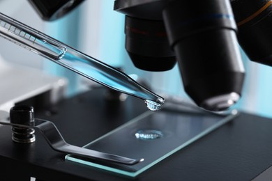 Photo of Dropping light blue liquid from pipette on glass slide in laboratory, closeup