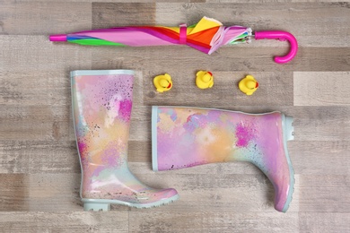 Pair of gumboots and umbrella on wooden background, top view. Female shoes