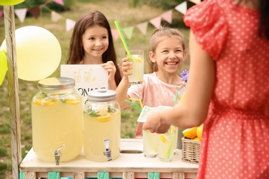 Little girls selling natural lemonade to woman at stand in park