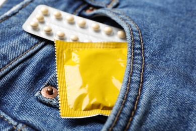 Yellow condom and birth control pills in pocket of jeans, closeup. Safe sex concept