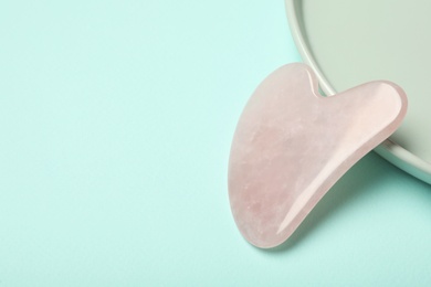 Photo of Rose quartz gua sha tool on turquoise background, space for text