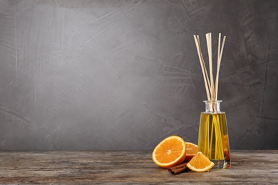 Aromatic reed air freshener, slice of orange and cinnamon stick on wooden table against grey background. Space for text