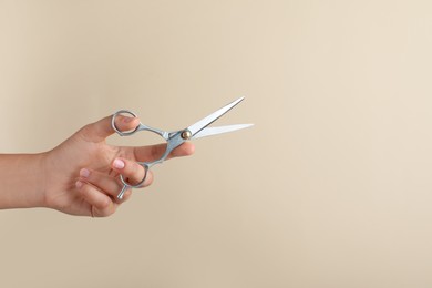Hairdresser holding professional scissors and space for text on beige background, closeup. Haircut tool
