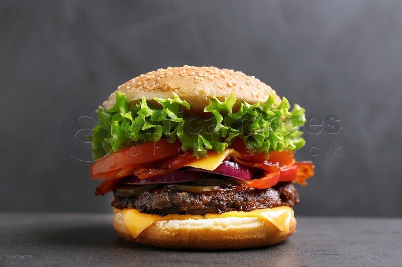 Photo of Tasty burger with bacon on table against grey background
