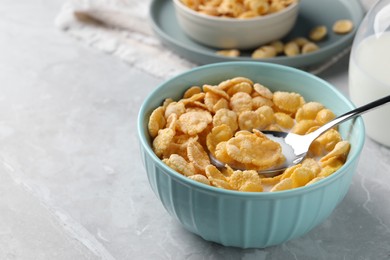 Spoon in bowl with tasty cornflakes and milk on light grey table, space for text