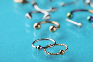 Photo of Stylish captive bead rings on light blue background, closeup. Piercing jewelry