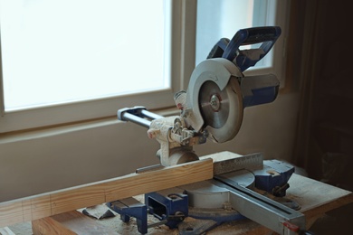 Carpenter's working place with modern circular saw near window indoors