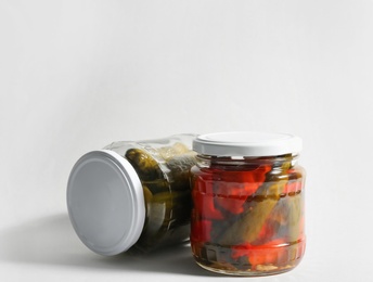 Glass jars with pickled bell peppers and cucumbers on white background